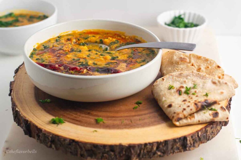 spinach dal in a white bowl with roti on the side