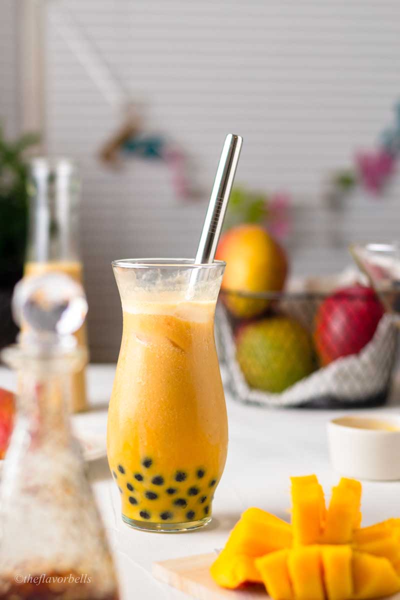 mango boba in a fancy glass with a basket of mango place on the side