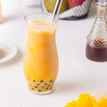 mango milk tea served in a glass with wide boba straw