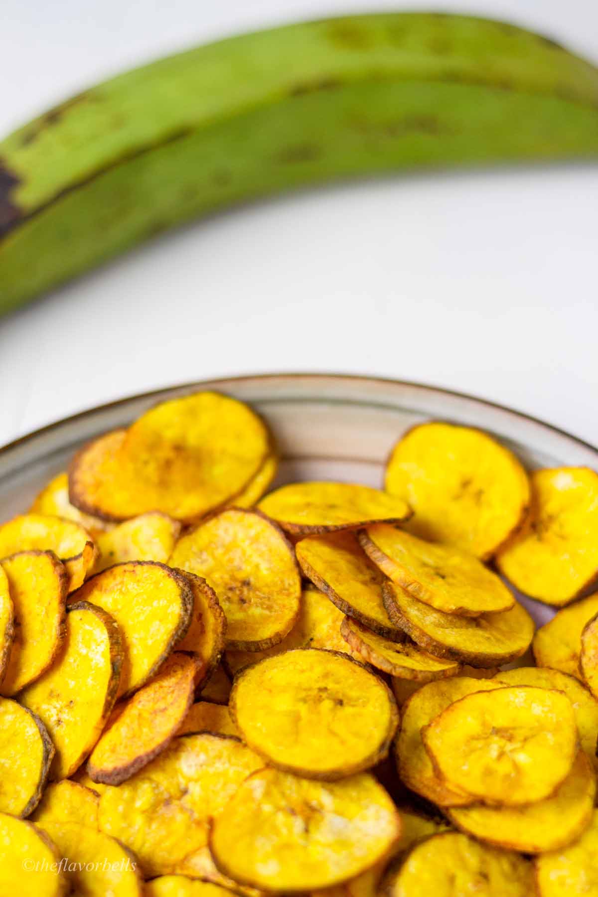 banana chips in a plate with green plantain in the background