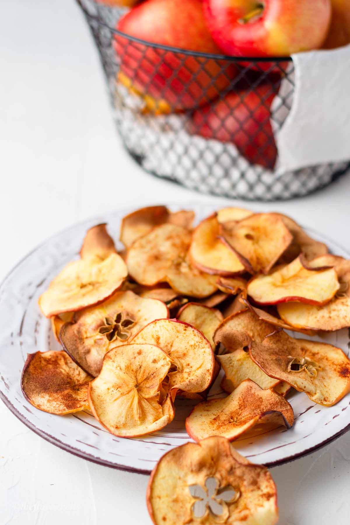 air fried apple chip in a plate with some apples in the background