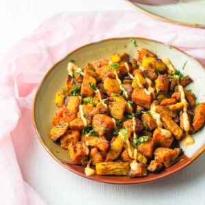 a plate of air fried sweet potato chunks with carrots drizzled with a dipping sauce and chopped herbs