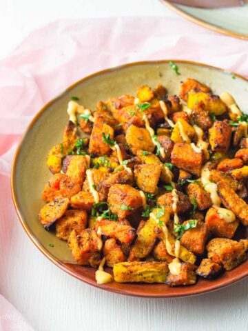 a plate of air fried sweet potato chunks with carrots drizzled with a dipping sauce and chopped herbs