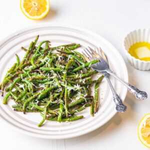 frozen green beans cooked in air fryer are being served with garted cheese, and a squeeze of lemon in a white plate