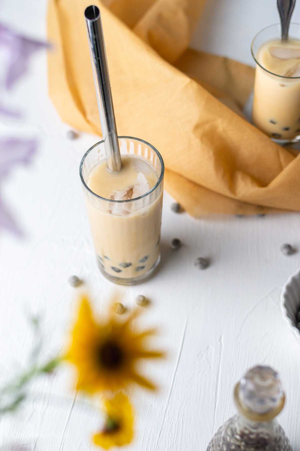 an overhead shot of the two glasses of caramel flavored milk tea, with a bloom of sunflower in the foreground