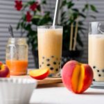 peach milk tea in glasses with peach slices and peaches around and peach syrup in background