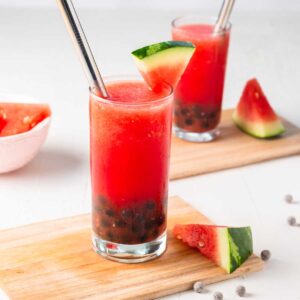 a glass of watermelon bubble tea with wide straw and a slice of watermelon