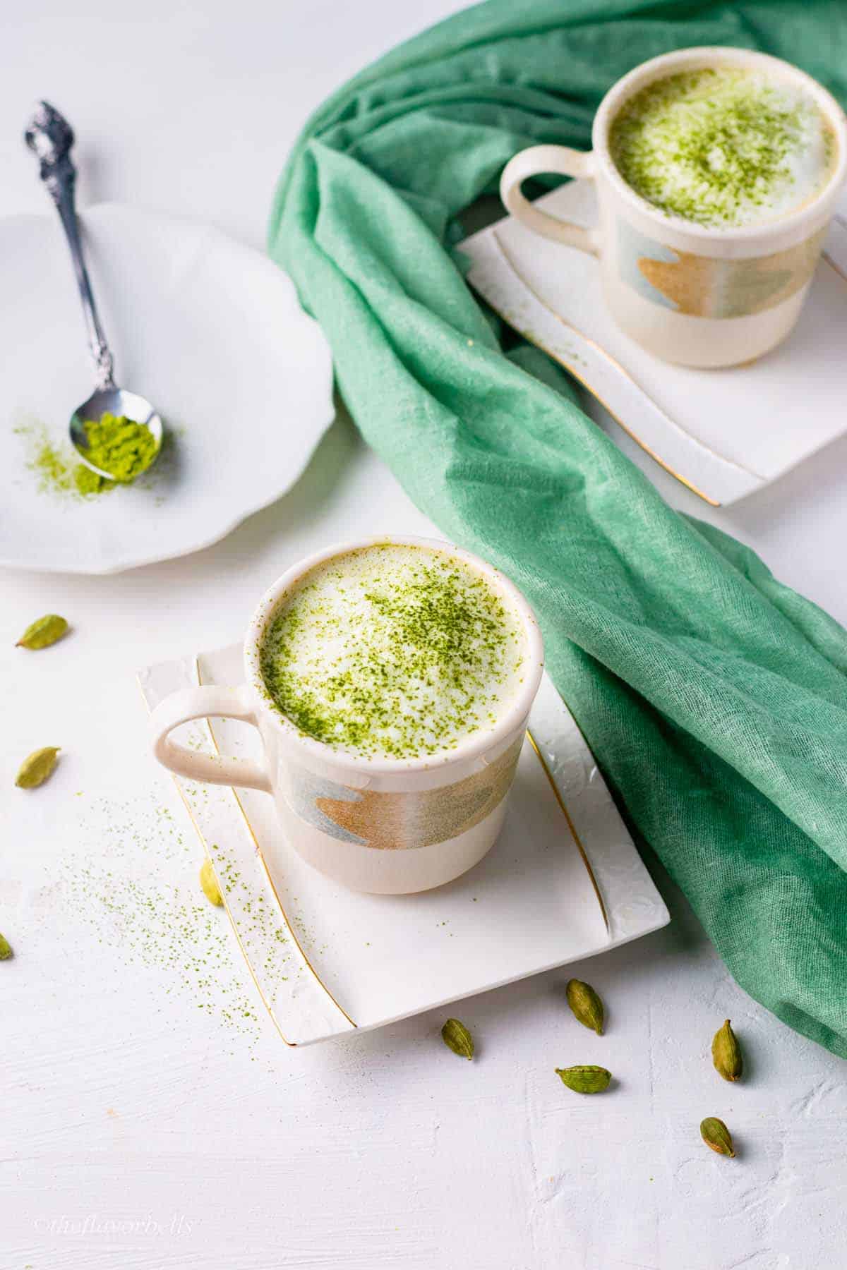 two cup of matcha latte with a spoon of matcha powder in the background
