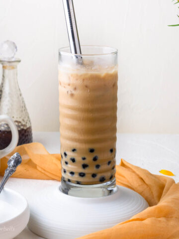 a glass of coffee boba with black tapioca pearls being added to it and a wide boba straw