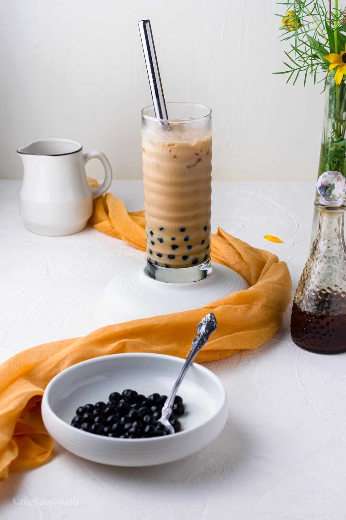 bubble tea made with a bowl of cooked black boba in the foreground and a glass of milk in the background.