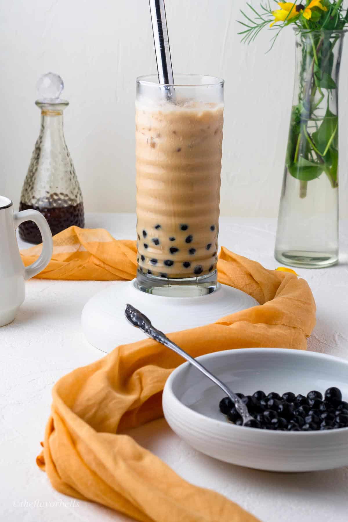 iced coffee with black tapioca pearls being served in a large glass with ice and a wide boba straw