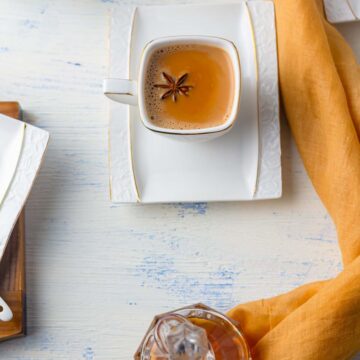 a cup of karak chai in a square cup saucer topped with a star anise