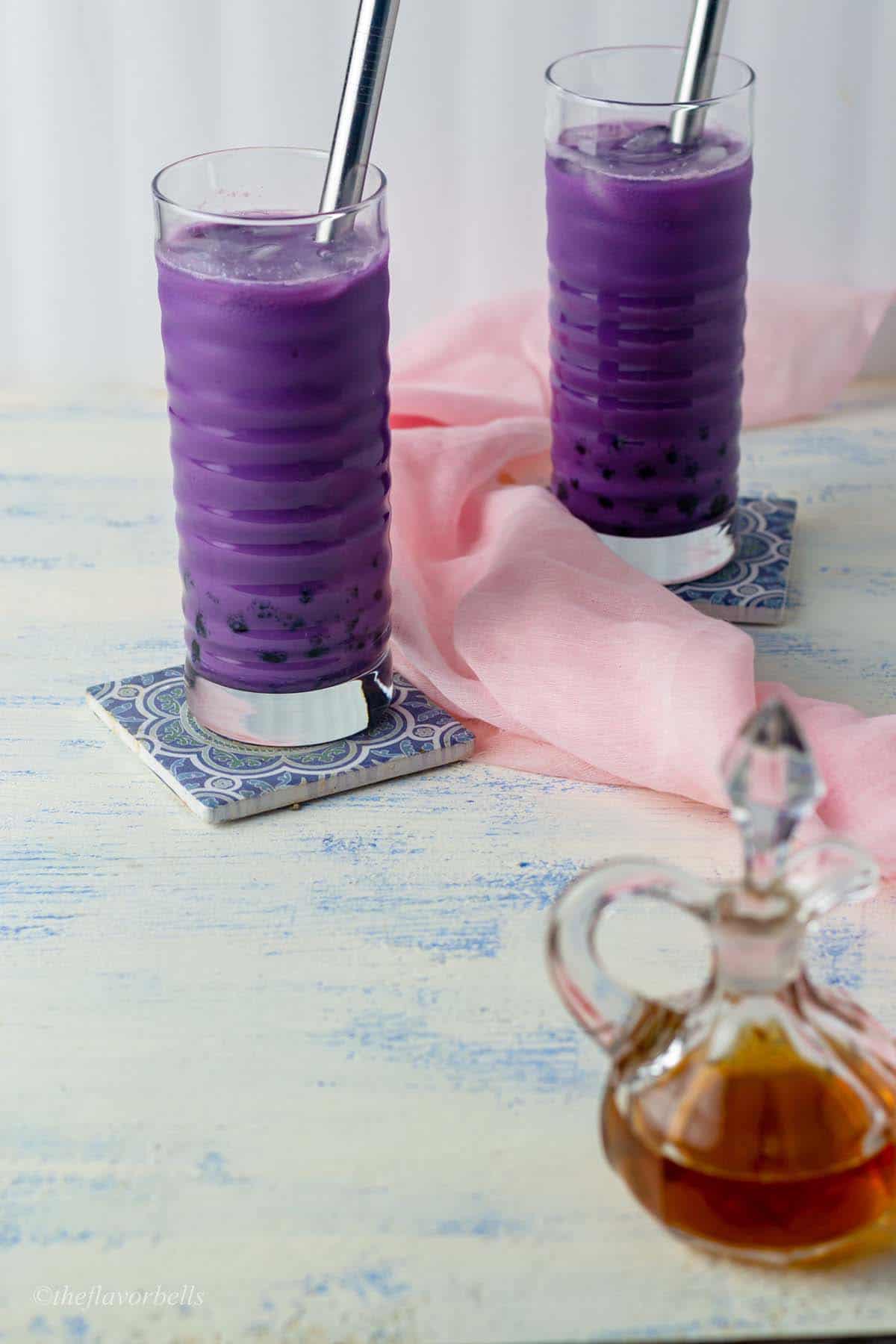 Two glasses of ube milk tea with a brown sugar syrup in the foreground