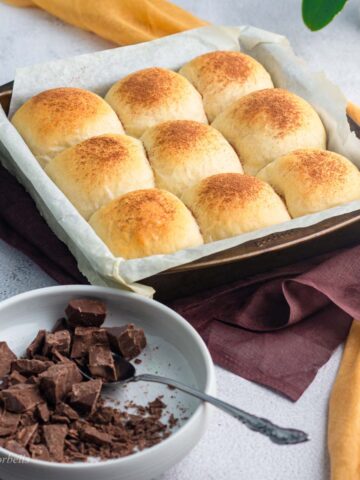 chocolate buns in a baking tray with some chocolate pieces places in a separate bowl