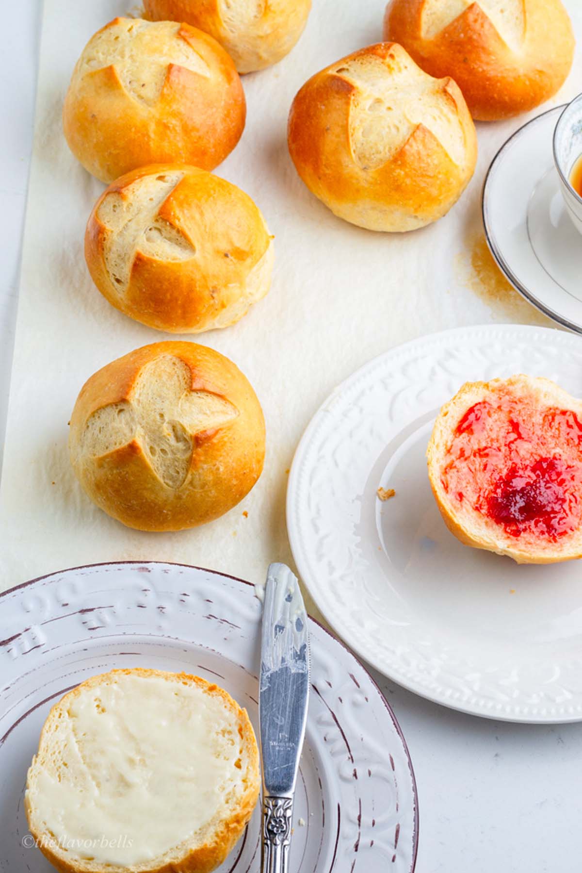 6 gorgeous crossed breakfast rolls placed on a parchment paper and a sliced bun on a white plate.