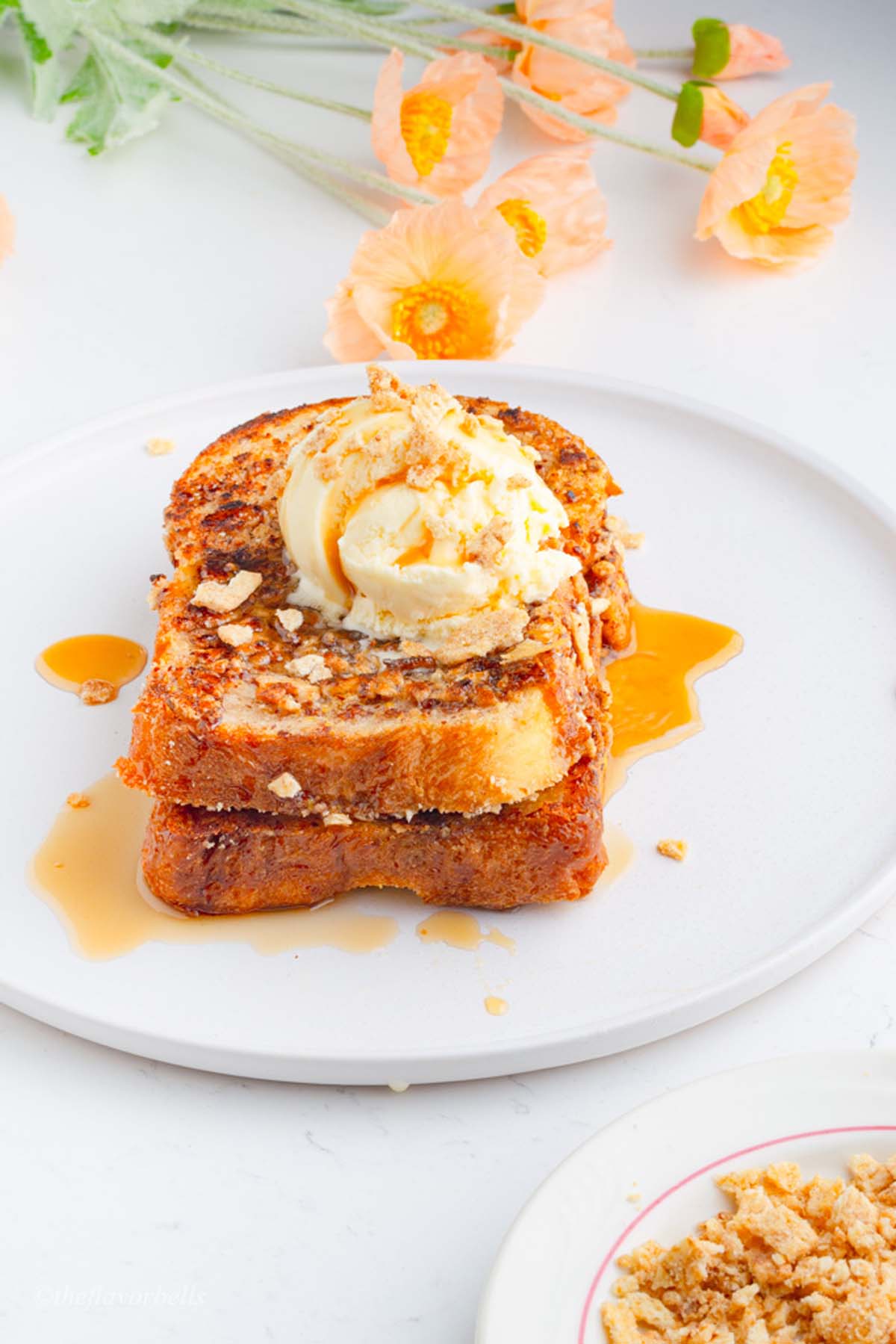 french toast served on a white plate with syrup and flowers in the background