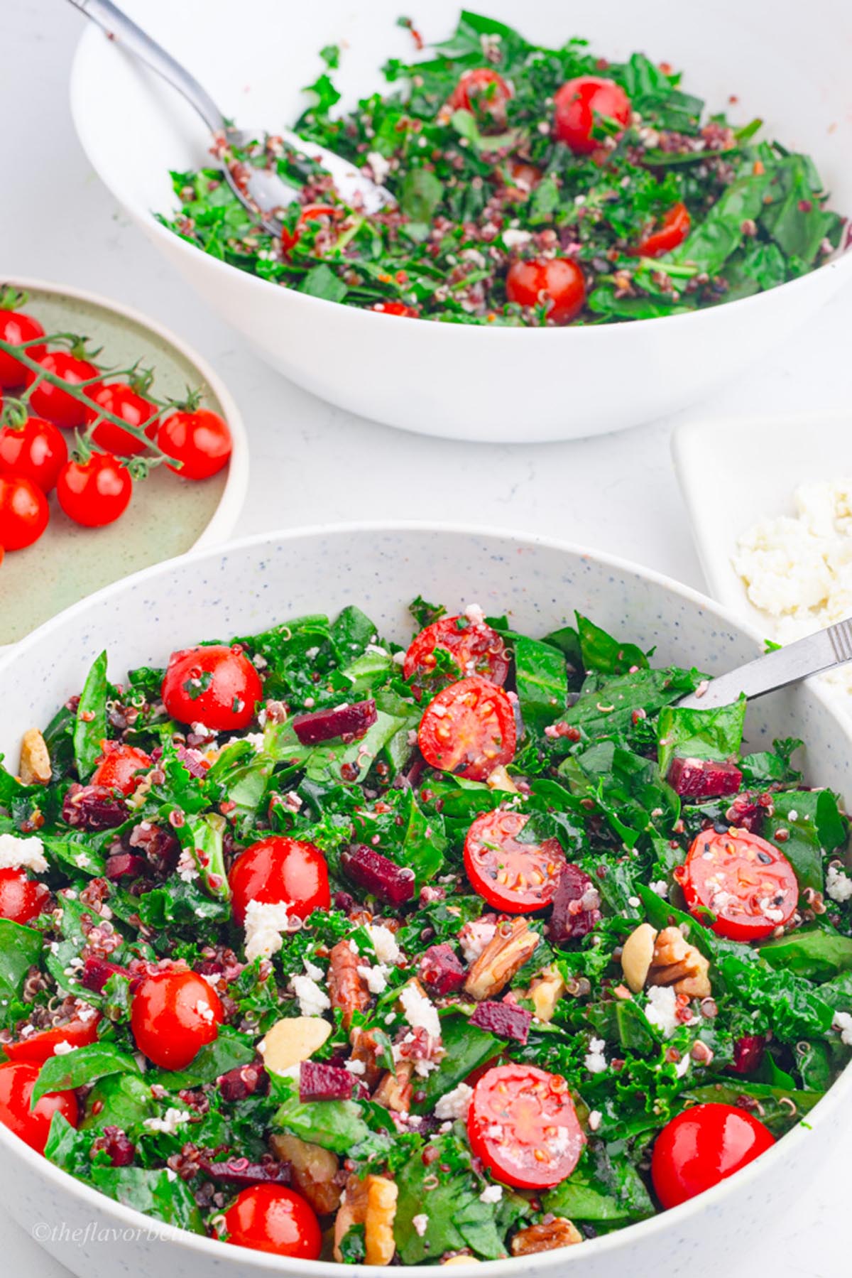 two bowls of vibrant kale and spinach salad with a bunch of ripe grape tomatoes in the background