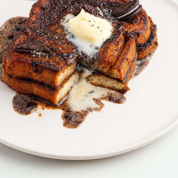 two slices of Oreo French Toast served in a white plate topped with Oreo pieces, scoop of vanilla, and Oreo icing