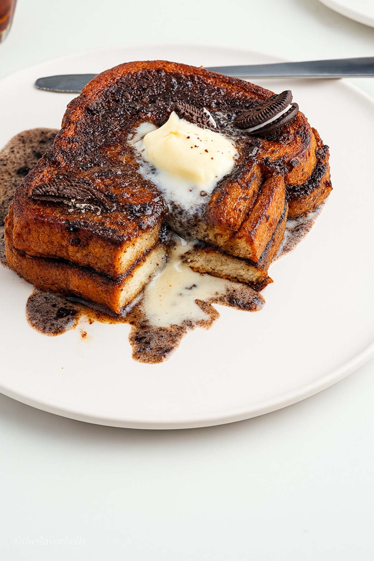 two slices of Oreo French Toast served in a white plate topped with Oreo pieces, scoop of vanilla, and Oreo icing
