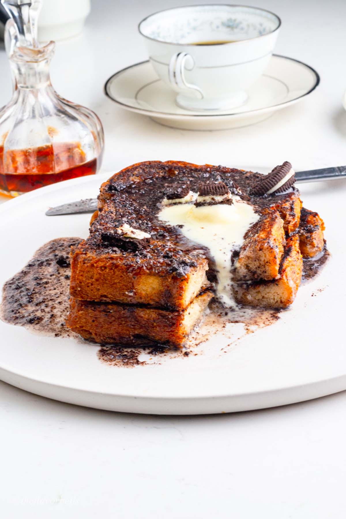 toast served with Oreo icing and topped with vanilla ice cream with a cup of tea in the background.