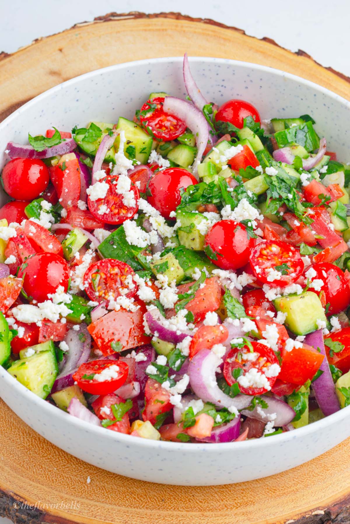 very colorful and fresh looking onion cucumber and tomato salad topped with crumbles feta and chopped parsley