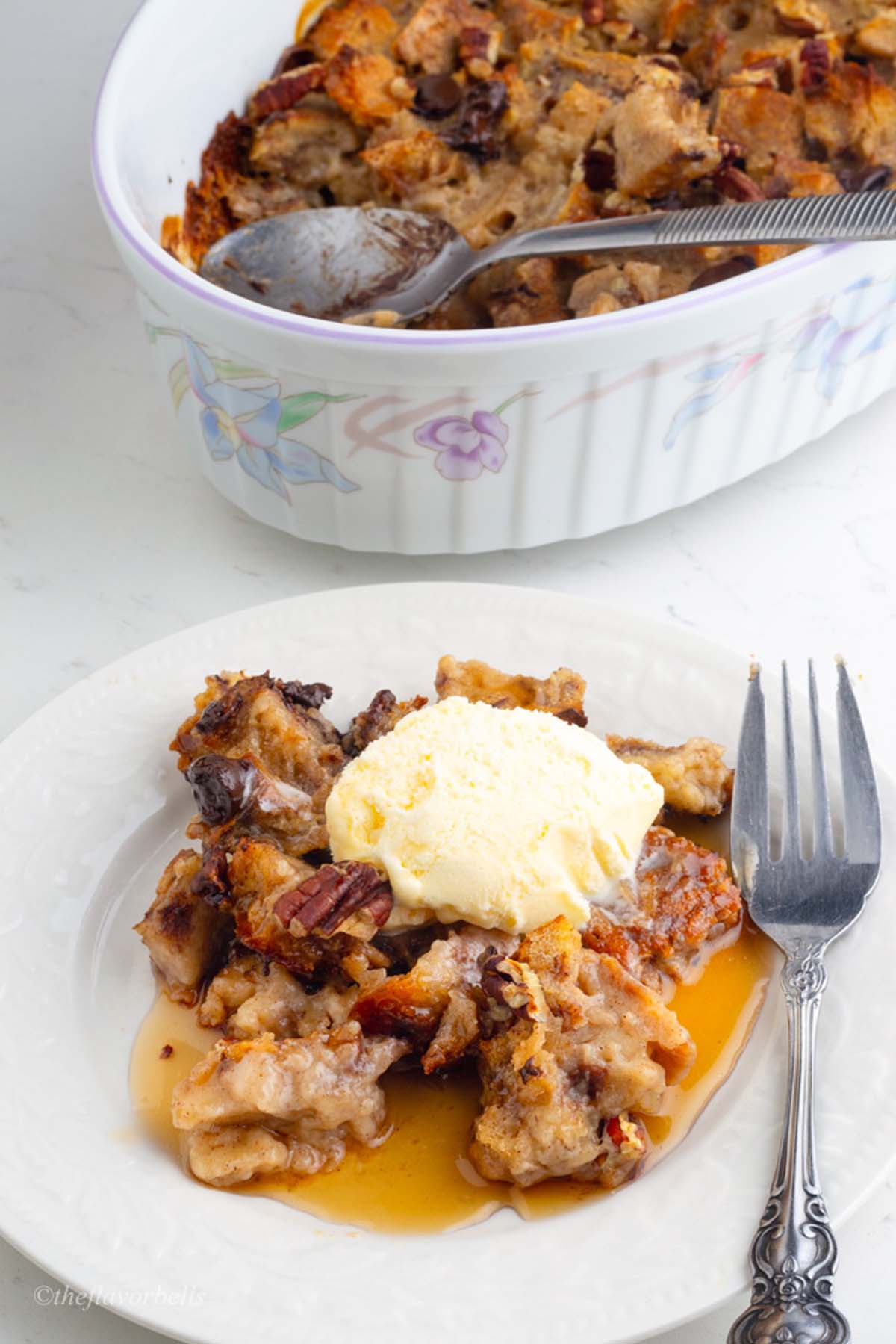 tempting plate of bread pudding with caramelized and custardy bread pieces topped with maple syrup and ice cream and nuts and choco-chips