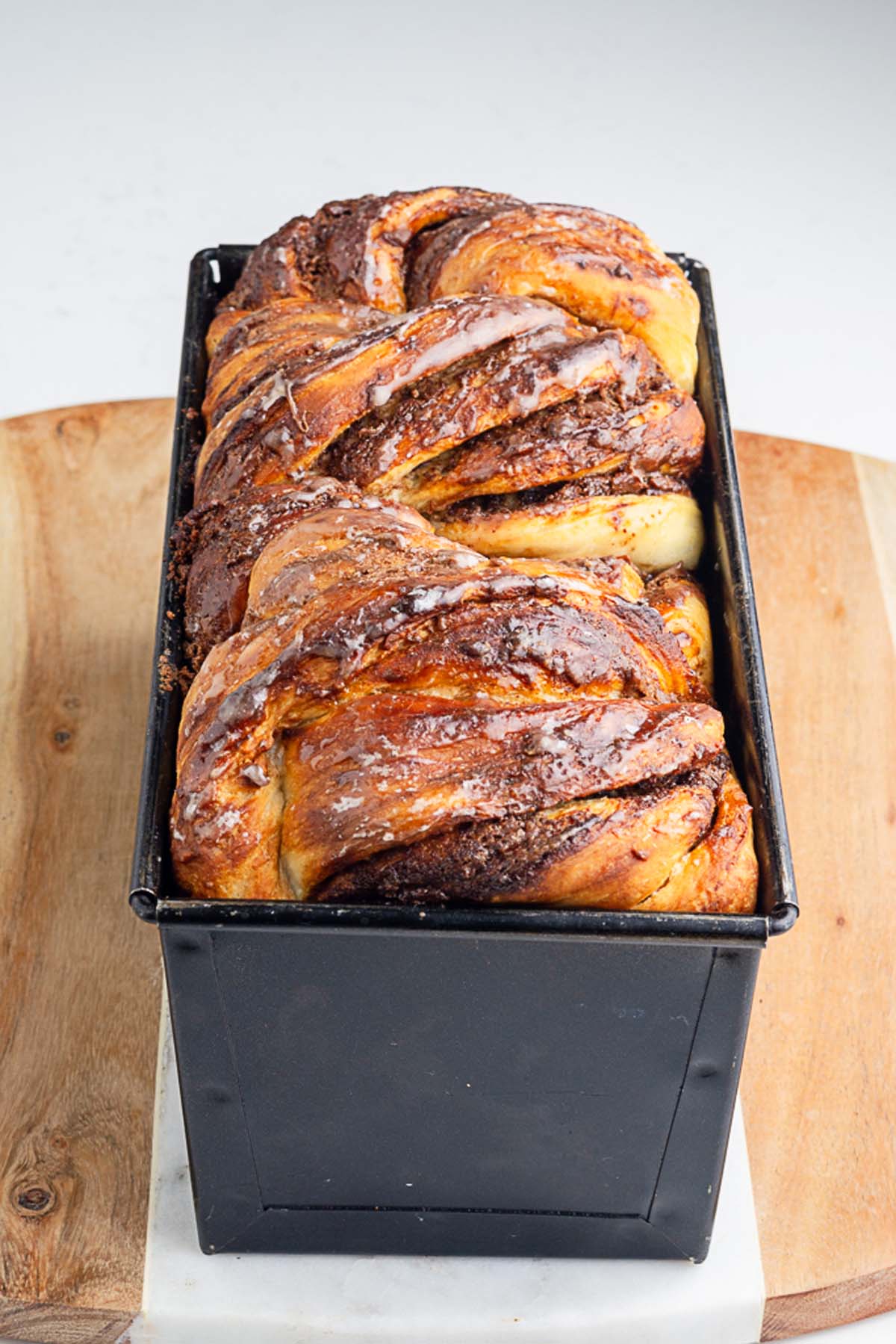 freshly baked loaf of babka in a loaf pan brushed with syrup