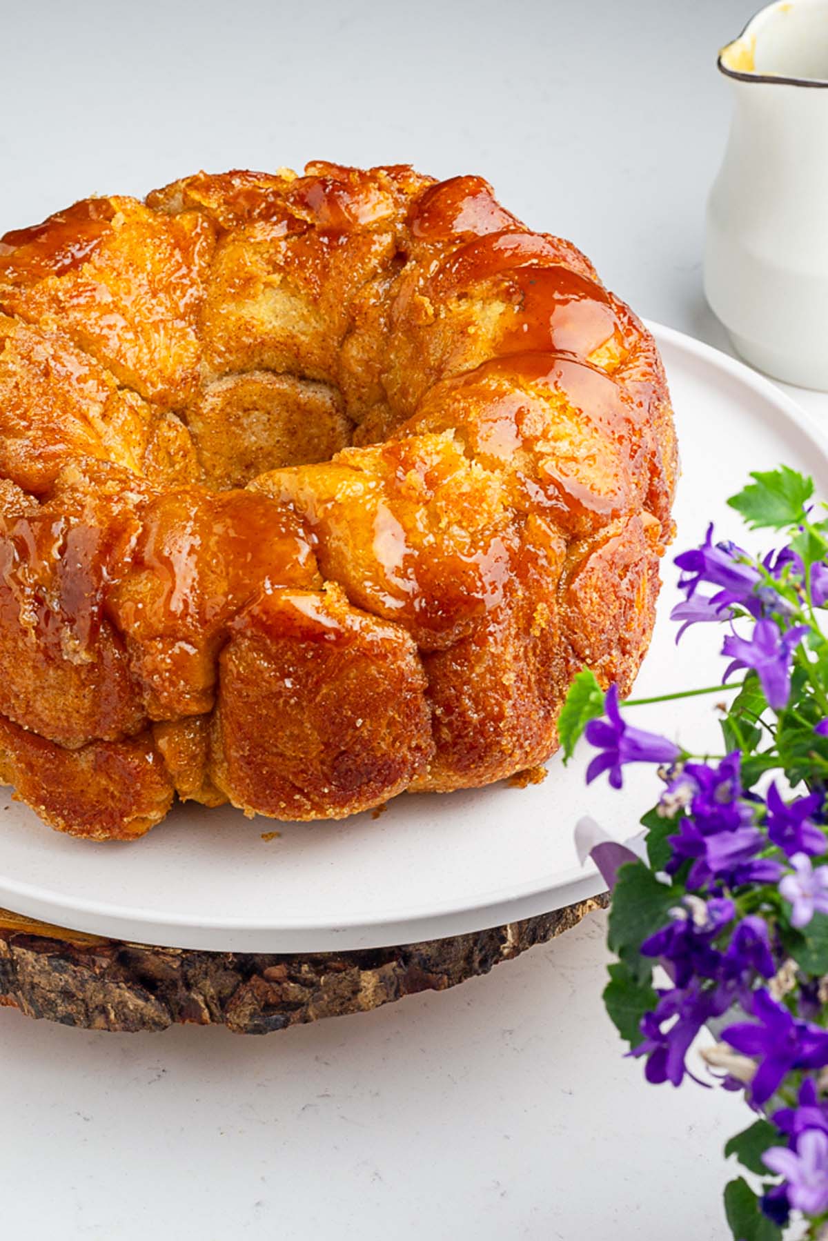 glossy and luscious pull apart sourdough monkey bread in a white plate with some purple flowers in the foreground