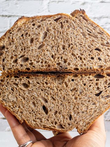 a loaf of 100 percent whole wheat sourdough bread sliced from center to show the rise of loaf and opne crumbs